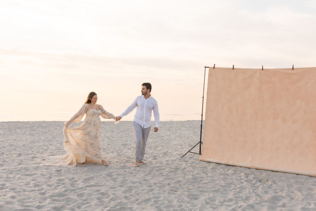 Expecting couple embracing on the beach during a Palm Beach maternity photoshoot, canvas backdrop