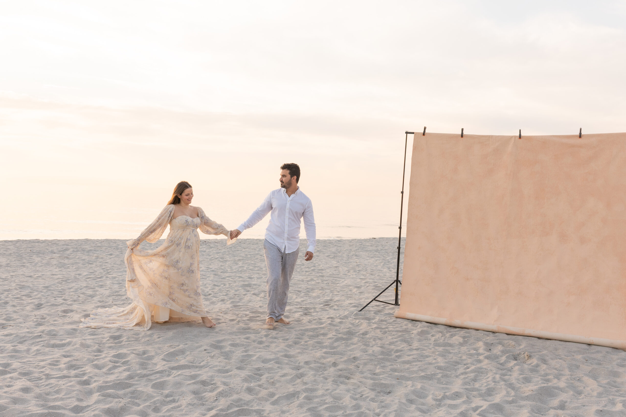 Expecting couple embracing on the beach during a Palm Beach maternity photoshoot, canvas backdrop